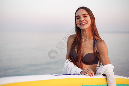 年轻姑娘在海滩上拿着桨板呢活动海洋女士冲浪者运动蓝色休闲假期享受海浪图片
