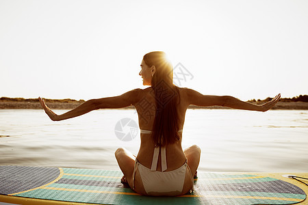 女人早上在桨板上练瑜伽的姿势女士晚饭身体冥想头脑冲浪天空日落海滩图片