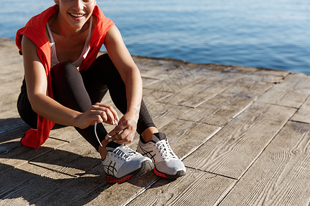 海上外出锻炼期间系鞋带的运动员妇女被割伤运动阳光成人行动慢跑者女性海洋训练赛跑者女孩图片