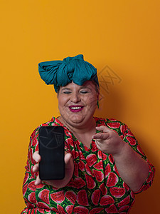 金发大个子女人在黄色背景下通过智能手机交谈 微笑着提出一个想法或问题 用快乐的脸指指点点 第一技术女孩细胞商业身体闲暇重量电话影图片