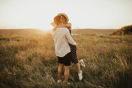 一个男人和一个戴着帽子的女人 拥抱和亲吻在草原上的高草地上太阳成年人假期热恋妻子夫妻情人女朋友丈夫新郎图片