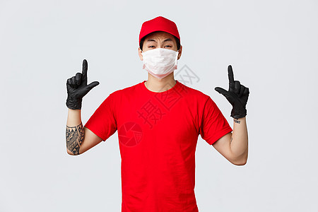 不情愿或害怕 缺乏安全感的亚洲人抱怨着 指着手指做鬼脸 穿着送货制服 红帽和 T 恤 公司用防护面具和手套保护人员健康服务快递食图片