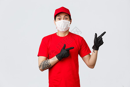 戴着医用口罩 防护手套和红色制服的亚洲送货员震惊并吓坏了 指指点点 身穿红色 T 恤和帽子的无语泰信使对某事感到焦虑 展示方式餐图片