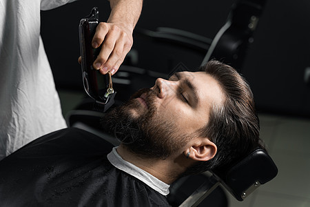 在理发店刮胡子 长着脚镣的理发师修剪英俊胡子的男人顾客工作室潮人商业主义剪刀理发绅士胡须头发图片