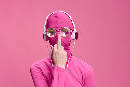 一个戴着面具和眼镜的粉红色背景中全粉红色男子的概念创意艺术照片 他正在用手的中指调整眼镜图片