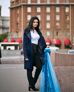 留着长长的黑发的迷人 体贴 穿着时髦的女人穿越欧洲 站在圣彼得堡市中心 一个美丽的女孩独自徘徊在秋天的街道上外套悲伤寂寞思考蓝色背景图片