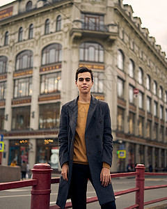 穿着优雅灰色大衣的黑发男子 在圣彼得堡历史中心街上站着 长着黑头发 厚眉毛的年轻人商业毛衣冒充青少年街道建筑学男人衣服男生成人图片