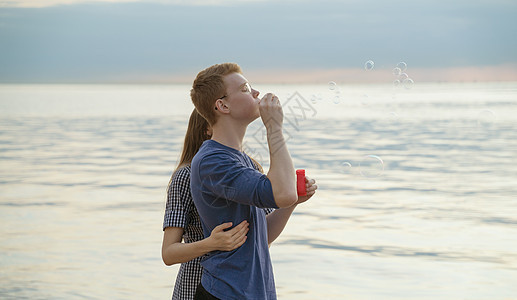 在海滩 海洋和天空上吹泡汤的 青少年情侣图片