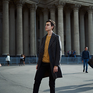 穿着优雅灰色大衣的黑发男子 在圣彼得堡历史中心街上站着 长着黑头发 厚眉毛的年轻人毛衣建筑学青少年冒充男生街道成人商业外套男人图片