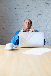 英俊英俊的成熟男人坐在笔记本电脑前的桌子旁听下属 窗前办公室里穿蓝色衬衫休闲服的男人 垂直图片