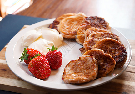白盘上加酸奶油的草莓煎饼和早餐餐桌图片