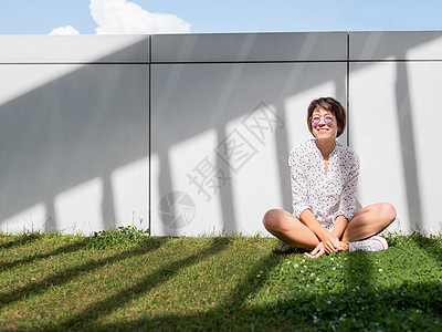 戴着彩色太阳镜的微笑女人在城市公园的草坪上休息 镇上的大自然 下班后到户外放松 夏日风情氛围季节性城市草地棕褐色天气乐趣眼镜阳光图片