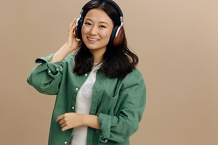享受这个声音吧 快乐可爱的亚洲学生年轻女孩穿着卡其绿色衬衫 触摸耳机 在米色糊面工作室背景上被孤立 很酷的时装报价 音乐应用平台图片