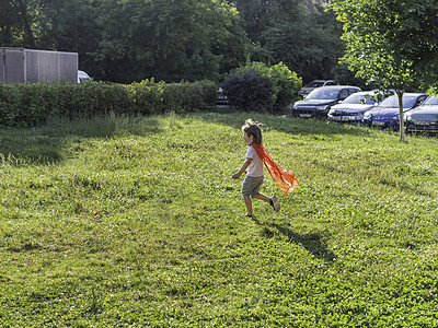 小男孩在草坪上扮演超级英雄 穿着手工制作的鲜红色斗篷的孩子 户外角色扮演游戏 阳光下的古装戏图片