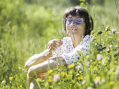 女人在多彩的太阳镜中 享受阳光和草地上的鲜花香味 夏天的感觉 户外放松 自我安慰日光场地植物女性晴天绿色季节性氛围背景图片