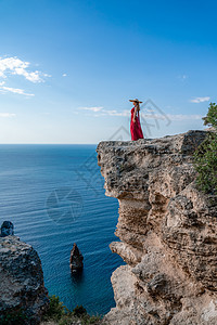 一个穿着红色飞行服的女人 在大海的背景下 飘在风中发抖着旅行太阳自由丝绸女孩尾巴女士幸福衣服女性图片