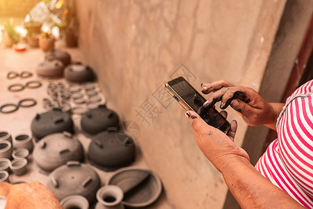 在尼加拉瓜拉巴斯中心的一个作坊里 工匠正在检查她的手机以进行在线销售 同时她的陶罐在阳光下晒干 贫穷国家的旅游 文化和经济概念图片