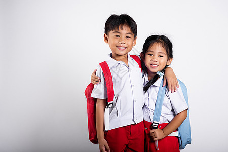 两个亚洲学生孩子女孩男孩小学生兄弟姐妹微笑快乐穿着学生泰国制服红色裤子裙子互相拥抱姐姐瞳孔衬衫朋友女学生童年兄弟会背包男生幼儿园图片