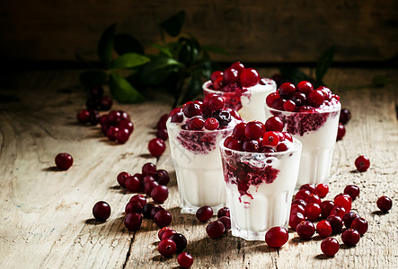 香草冰淇淋甜点 配蔓越莓酱和浆果新鲜蔓越莓 在旧木背景的小玻璃杯中供应 有选择的焦点图片