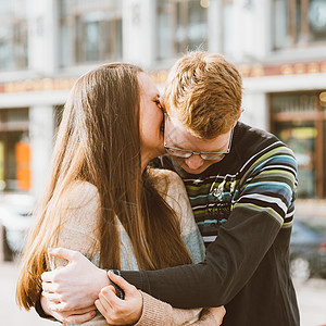 幸福的情侣在市中心拥抱的画像 戴着眼镜的红发男人亲吻着 女人留着长发 女孩在男人耳边低语 青少年爱情和初吻 爱情 关系 情侣的概图片