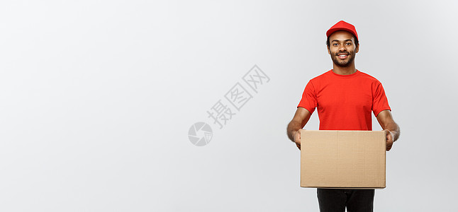 送货概念快乐的非洲裔美国人送货员的画像 穿着红布拿着盒子包裹 隔绝在灰色演播室背景 复制空间职业工作室红色衣服礼物男生经销商成人图片