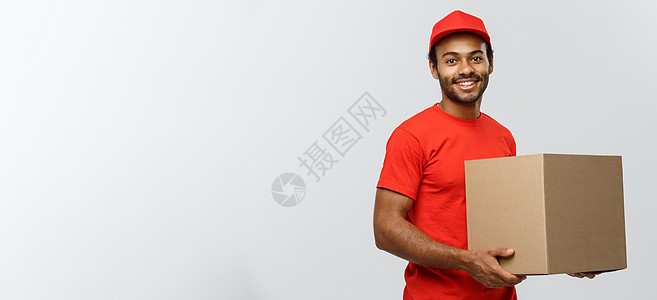 送货概念快乐的非洲裔美国人送货员的画像 穿着红布拿着盒子包裹 隔绝在灰色演播室背景 复制空间工人导游商业礼物衣服工作室成人红色相图片