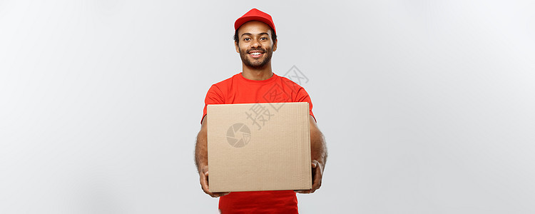 送货概念快乐的非洲裔美国人送货员的画像 穿着红布拿着盒子包裹 隔绝在灰色演播室背景 复制空间照片导游邮递员红色成人职业礼物男性工图片