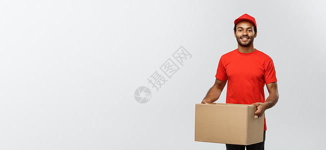 送货概念快乐的非洲裔美国人送货员的画像 穿着红布拿着盒子包裹 隔绝在灰色演播室背景 复制空间商业照片男生邮递员礼物红色职业经销商图片