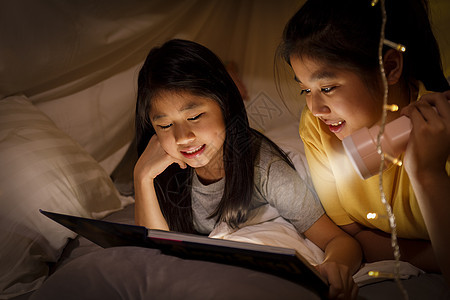 家庭观念 姐姐和姐姐睡前在儿童帐篷里用手电筒看书 快乐的姐姐在床单帐篷里给姐姐读故事书女儿游戏室婴儿女孩阅读孩子们幸福卧室童年说图片