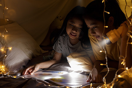 家庭观念 睡前姐姐和姐姐一起用手电筒看书 姐姐在床单帐篷里一起读故事书 重点选择性小姐姐 具有胶片颗粒效果孩子们父母闲暇妹妹童年背景图片