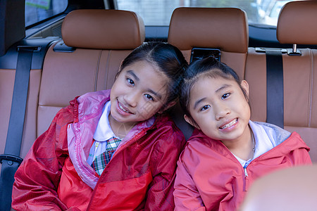 两个快乐的学生在享受汽车公路旅行时微笑着 早上 姐妹们微笑着看着车内的相机 在去学校的路上坐在车里的亚洲孩子 车里的一家人图片