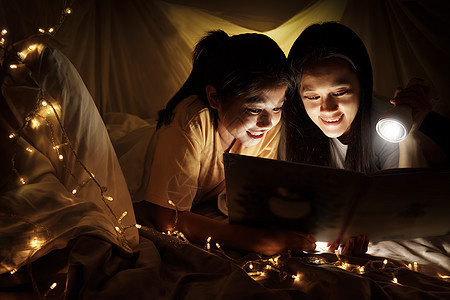 家庭观念 睡前 母亲和孩子的女儿在儿童帐篷里用手电筒一起看书 快乐的妈妈在床单帐篷里给女儿读故事书房间阅读女性故事喜悦游戏室乐趣图片