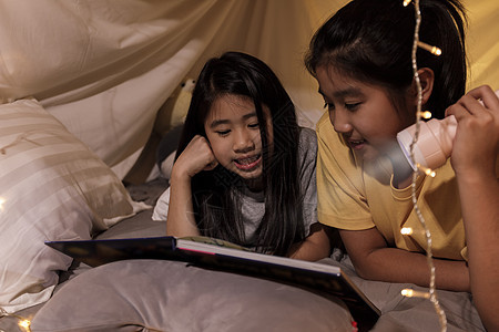 家庭观念 姐姐和姐姐睡前在儿童帐篷里用手电筒看书 快乐的姐姐在床单帐篷里给姐姐读故事书孩子们就寝卧室毯子阅读被单学习童年游戏室女图片