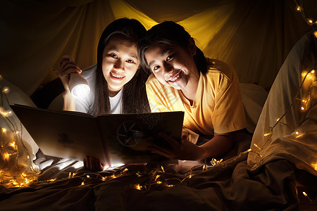 家庭观念 睡前 母亲和孩子的女儿在儿童帐篷里用手电筒一起看书 快乐的妈妈在床单帐篷里给女儿读故事书教育学习就寝被单卧室女孩婴儿时图片