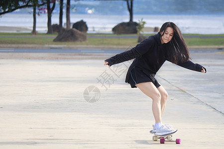 溜滑板的女孩美丽的夏日 亚洲女性在户外玩滑冰板 早上 快乐的年轻女性在公园玩冲浪板 体育活动生活方式概念 年轻女性喜欢使用 SurfSkat背景