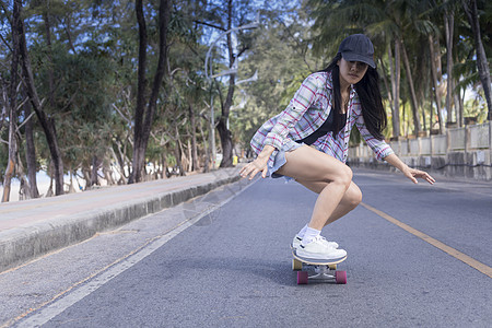 年轻的亚洲女性早上在户外的海滩路上玩冲浪滑板 快乐的女人在海滩路上玩滑板 体育活动生活方式概念享受女孩公园森林街道溜冰者滚筒运动图片