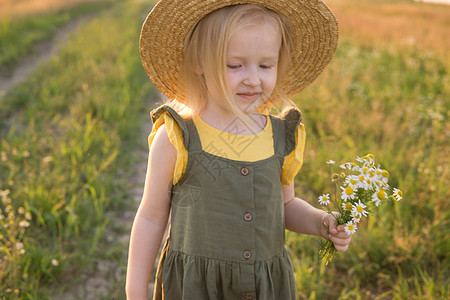 一个戴着草帽的金发小女孩拿着一束雏菊走在田野里 走在自然 自由和生态友好型生活方式中的概念过敏场地帽子乐趣阳光花束环境植物野生动图片