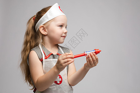穿着医生制服 带着玩具注射器看着摄像机的可爱小可爱滑稽女孩玩耍情感女性娱乐欢乐眼镜冒充卫生职业喜悦治疗师图片