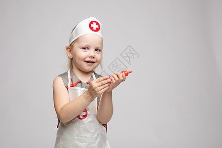 穿着医生制服 带着玩具注射器看着摄像机的可爱小可爱滑稽女孩玩耍童年情感乐趣享受治疗师护士娱乐眼镜快乐工作室图片