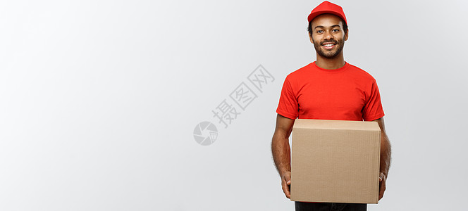送货概念快乐的非洲裔美国人送货员的画像 穿着红布拿着盒子包裹 隔绝在灰色演播室背景 复制空间男性礼物男生照片工人相机导游商业经销图片