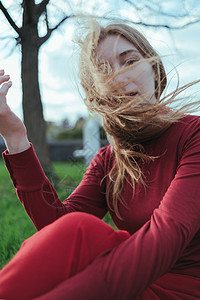 城里一个穿红衣服的金发女孩 在城市里坐着 头发是风吹成的眼睛公园晴天女士裙子植物群金发女郎缠绕天空衬套图片