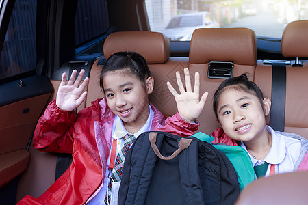 两个快乐的学生在享受汽车公路旅行的同时举手和动作 早上 姐妹们微笑着看着车内的相机 在去学校的路上坐在车里的亚洲孩子 车里的一家图片