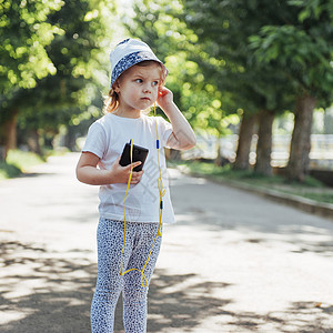 在户外用耳机听音乐的可爱女孩孩子头巾冒充童年头发微笑衣服背景图片