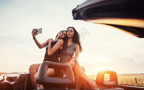 年轻两个女青年在拍照时拍照片 女孩们乐于摆姿势成人乐趣执照车辆敞篷车女性女士青少年日落女孩图片