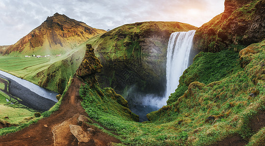冰岛南部靠近冰岛的Skogafos大瀑布阳光薄雾环境悬崖岩石老年天空衬衫溪流游客图片