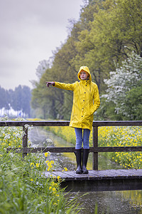 春生带黄雨衣和橡胶靴的年轻女青年公园衣服雨鞋女士橡皮鞋类天气下雨女孩裙子背景图片