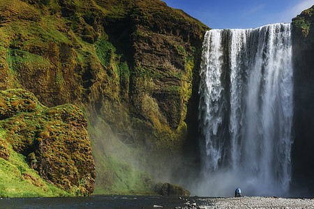 冰岛南部靠近冰岛的Skogafos大瀑布旅行悬崖阳光天空蓝色男人衬衫薄雾岩石环境图片