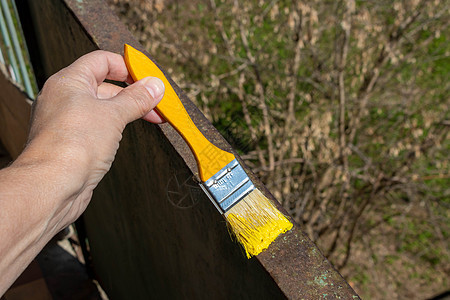 在阳光明媚的一天 一只手拿着黄刷子画着阳台上生锈的铁栏杆图片