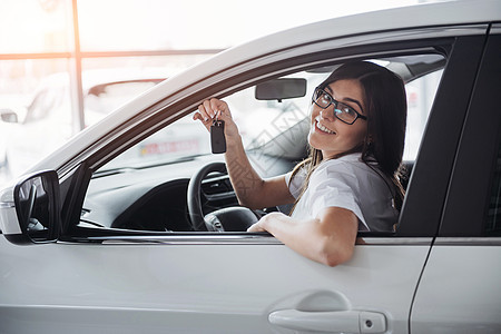 在车旁边的年轻快乐的女人 手握着钥匙政策车库车辆发动机交通机械服务巡航经销商零售图片