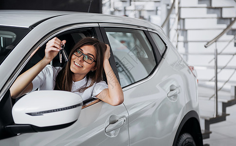 在车旁边的年轻快乐的女人 手握着钥匙车辆零售商业保险发动机女孩测试奢华女士微笑图片